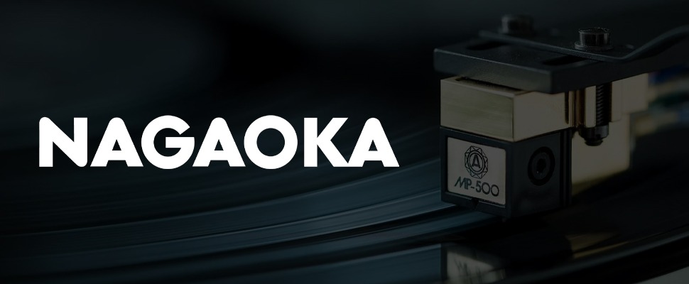 Close-up of a Nagaoka MP-500 cartridge playing a vinyl record, with the brand name "NAGAOKA" in bold white text on the left. The scene conveys precision and high-quality audio.