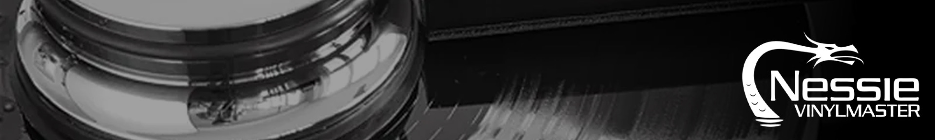 Close-up of a black and white vinyl record with a shiny metal component. "Nessie Vinylmaster" logo featuring a stylized serpent is on the right.