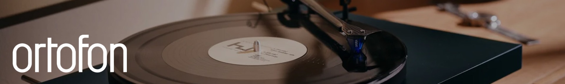 Close-up of a vinyl record playing on a turntable with "ortofon" branding. The needle is on the record, conveying nostalgia and music appreciation.