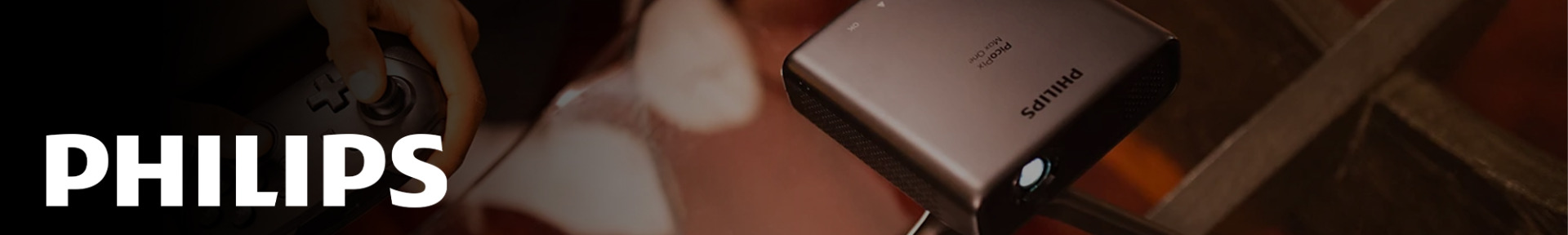 A Philips mini projector sits on a table, projecting light. A hand holds a game controller nearby. The scene conveys technology and entertainment integration.