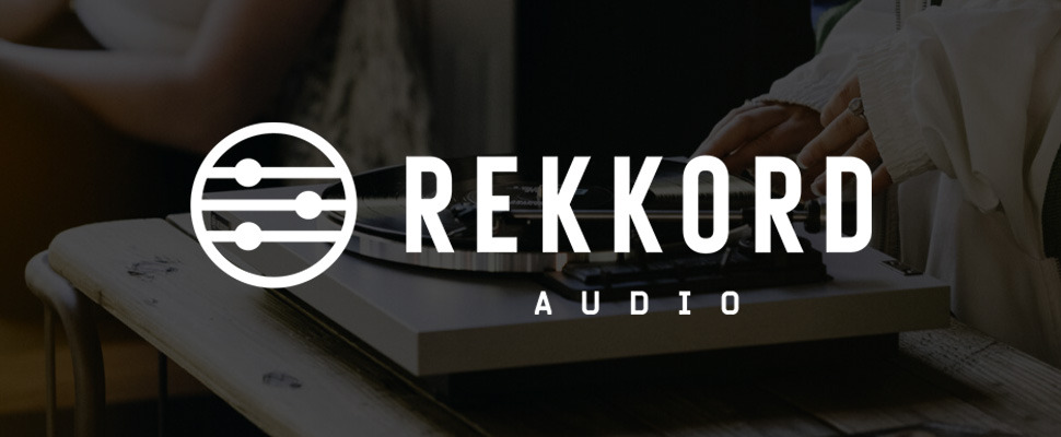 Close-up of a vinyl record being placed on a turntable. The background features the logo and text 'REKKORD AUDIO.' The scene conveys a sense of vintage nostalgia and music appreciation.
