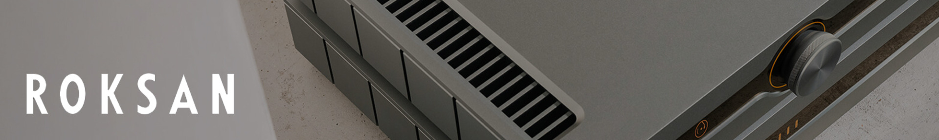 Close-up of a sleek, modern audio amplifier with a metallic surface and air vents, next to the stylized white text 'Roksan' on a grey background