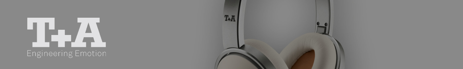 Close-up of stylish headphones with a metal finish and soft ear pads on the right; "T+A Engineering Emotion" text in white on a grey background to the left.