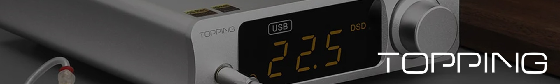 A sleek, silver audio device with a digital display shows "22.5." It’s connected via a cable, conveying a high-tech, modern feel. The word "TOPPING" appears prominently.