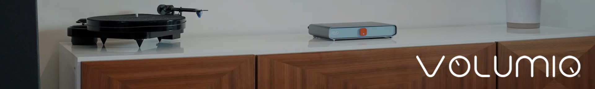 Modern audio setup with a turntable on a sleek white surface and a compact audio device beside it, resting on a wooden cabinet. The word "Volumio" is displayed.