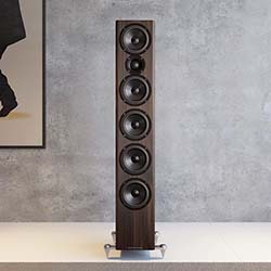 A modern living room features a tall black speaker centred on a wooden floor, with a monochrome pop art portrait on the wall. The room has a minimalist and stylish feel.