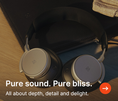 A pair of sleek, gray over-ear headphones resting on a wooden surface with a leather pouch. Text overlay reads "Pure sound. Pure bliss."