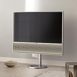 A flat-screen TV on a sleek stand in a modern living room, set against a light gray wall. Nearby is a small round bowl, conveying a minimalist aesthetic.