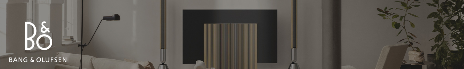 Modern living room with minimalist decor. Features tall speakers, a sleek TV, stylish lighting, and lush plants. Bang & Olufsen logo displayed.