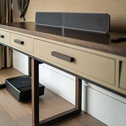 Modern desk with sleek black soundbar on top and beige drawers beneath. Wooden floor and minimalist décor create a calm, tidy atmosphere.