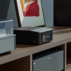 A sleek black Node Icon sits on a wooden shelf, next to a colourful abstract painting. The scene is modern, minimalist, and stylish.