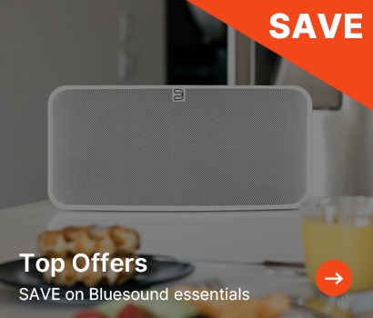 Rectangular grey speaker on a white table with breakfast items. Bold orange 'SAVE' banner and text promoting Bluesound offers.