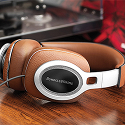 Brown leather Bowers & Wilkins over-ear headphones rest on a wooden surface, with a blurred turntable in the background, conveying a vintage audio vibe.