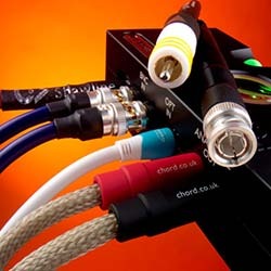 Close-up of colourful audio cables connected to a black device against an orange background, showcasing modern technology and connectivity.