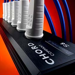 Close-up of a sleek black power strip labelled "Chord Company." It has white outlets and blue cords against a vibrant orange background.