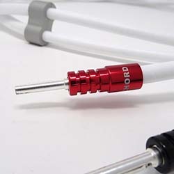 Close-up of a white audio cable with a red metallic connector labelled "CHORD," lying on a white surface. An out-of-focus black connector is in the foreground.