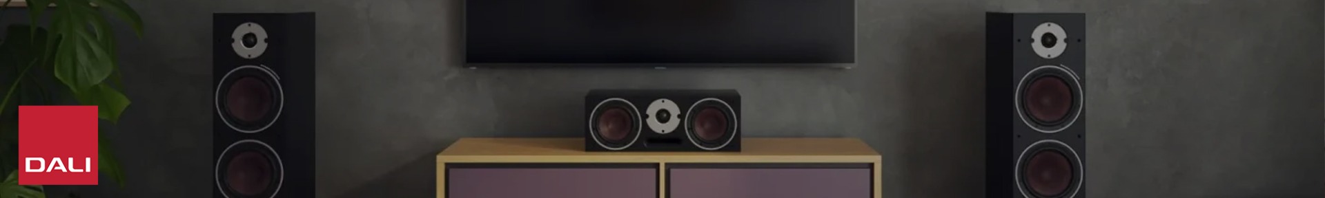 A modern living room with two large black speakers and a matching centre speaker beneath a wall-mounted TV.