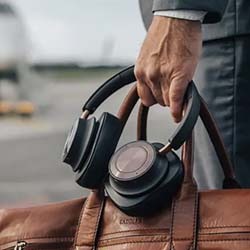 A hand holds black headphones and a brown leather bag at an airport.