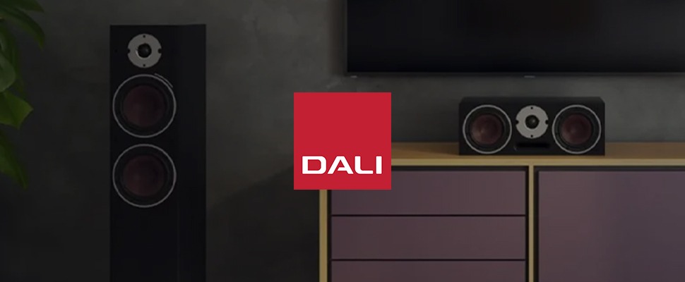 A modern living room with two large black speakers and a matching centre speaker beneath a wall-mounted TV.