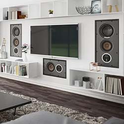 Modern living room with a sleek white entertainment unit featuring a large flat-screen TV and built-in speakers. Shelves hold books and décor, creating a cosy atmosphere.