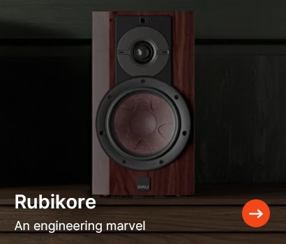 A sleek wooden speaker with a large circular woofer and smaller tweeter, set on a dark wooden surface. Text: "Rubikore, An engineering marvel."