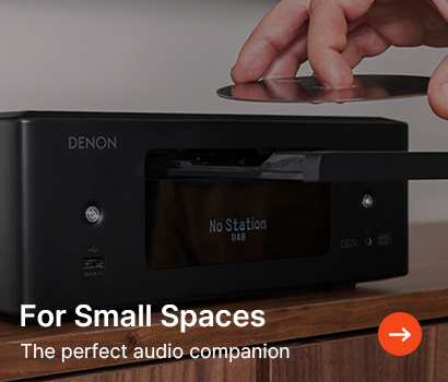 Hand inserting a CD into a compact Denon audio system on a wooden surface. The text reads, "For Small Spaces: The perfect audio companion." Tone is sleek and modern.