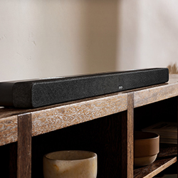 Sleek black soundbar on a wooden shelf with decorative bowls beneath. The setting is cosy, blending modern technology with rustic décor.