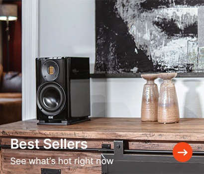 A modern black speaker sits on a wooden table beside two ceramic vases. Abstract art hangs on the wall. Text overlay: "Best Sellers, See what's hot right now."