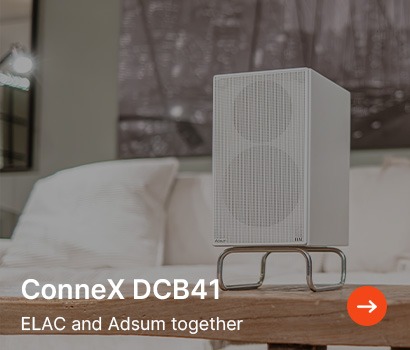 A sleek, modern ELAC ConneX DCB41 speaker sits on a wooden table against a blurred couch backdrop. Text reads, "ConneX DCB41, ELAC and Adsum together."