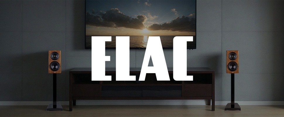 A minimalist living room features two wooden ELAC speakers flanking a TV displaying a serene ocean sunset, creating a calm and sophisticated atmosphere.