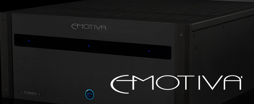 Close-up of a black Emotiva audio amplifier with a sleek design, featuring the brand's logo in white and subtle blue indicator lights on the front.
