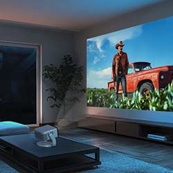 A cozy living room with a large projector screen showing a cowboy beside a red truck in a field. The room is dimly lit, with a couch and a coffee table.