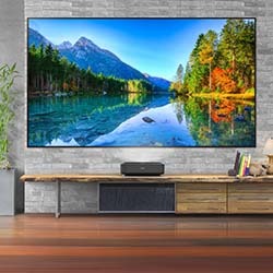 Large flat-screen TV on stone wall showing vibrant lake and forest scene, autumn colours. Below, a modern console table and décor create a cosy, inviting space.