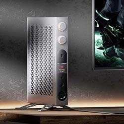 A sleek, silver DAC sits on a wooden desk beside a monitor displaying a dark fantasy image, creating a modern, tech-focused aesthetic.