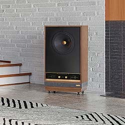 A vintage-style speaker with wood panelling and large black front stands on a patterned rug in a modern room with white brick and wood accents.