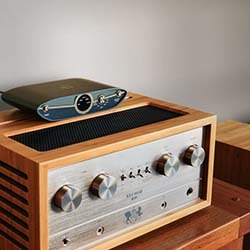 A vintage wooden stereo receiver with metallic knobs sits on a wooden table. A modern audio interface rests on top, blending old and new technology.