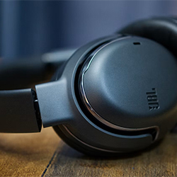 Close-up of black over-ear headphones resting on a wooden surface, showcasing a sleek design. The background is softly blurred, adding a modern touch.