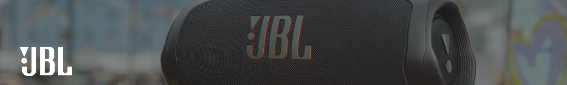 Close-up of a black JBL portable speaker with the JBL logo prominently displayed. The background is a blurred graffiti wall, creating an urban vibe.