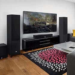 A modern stereo system with a digital display sits atop a wooden shelf. Below it is a sleek speaker with multiple drivers. Books and décor are neatly arranged.