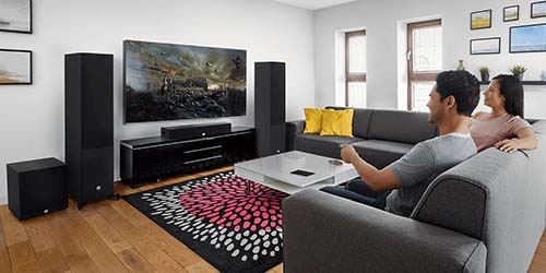 A modern stereo system with a digital display sits atop a wooden shelf. Below it is a sleek speaker with multiple drivers. Books and décor are neatly arranged.