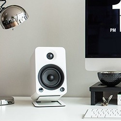 A modern desk setup with a white speaker, silver lamp, and computer screen.