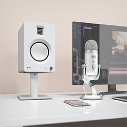 A modern workspace with a white speaker, a sleek microphone, a smartphone on a desk, and a monitor displaying video editing software