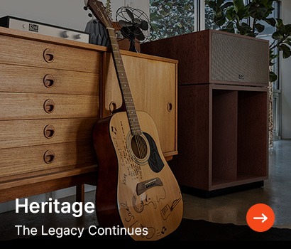 A wooden acoustic guitar leans against a vintage sideboard with large speakers nearby. Text reads "Heritage: The Legacy Continues." Warm and nostalgic tone.