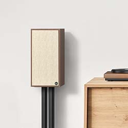Vintage-style speaker with a wooden frame and beige fabric cover on a stand. A wooden cabinet holds a turntable. Minimalist and retro vibe.