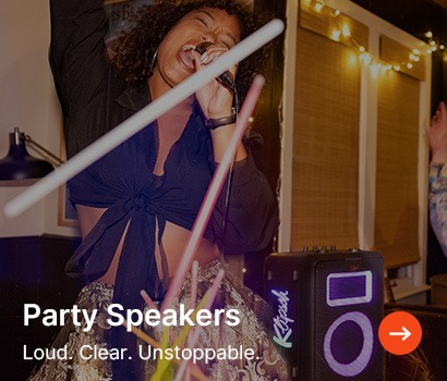 A woman singing passionately into a microphone at a lively party, surrounded by glowing lights and a speaker. Text reads: "Party Speakers. Loud. Clear. Unstoppable."