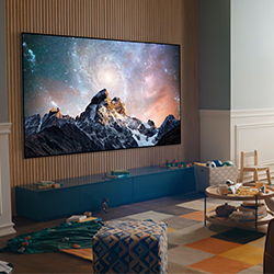 Living room with a large TV showing a mountain and starry sky. Cosy setting includes a colourful rug, toys, and a small chair, creating a warm atmosphere.