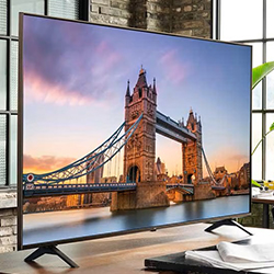 A sleek flat-screen TV displays Tower Bridge under a vibrant sunset. The modern décor and bright natural light from large windows create a warm ambiance.