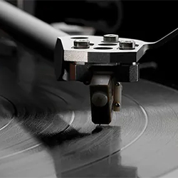 Turntable close-up with a needle on a vinyl record, emphasizing grooves and texture. The image conveys a sense of nostalgia and vintage audio.