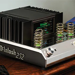 Alt text: High-end McIntosh 252 amplifier on a wooden table, featuring exposed vacuum tubes with a green glow, sleek design, and metallic finish.