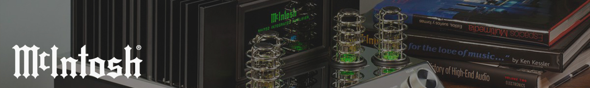 Close-up of a McIntosh audio amplifier with glowing tubes and green display, placed beside stacked books on high-end audio, creating a vintage, sophisticated atmosphere.